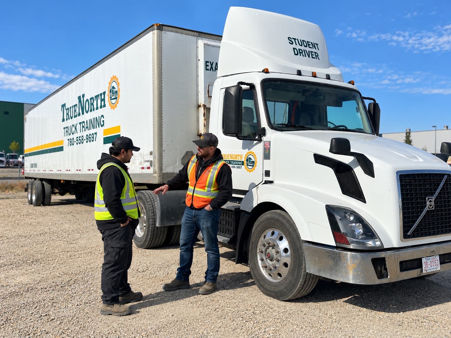 Instructor talking with a student beside a white Student Driver tractor-trailer